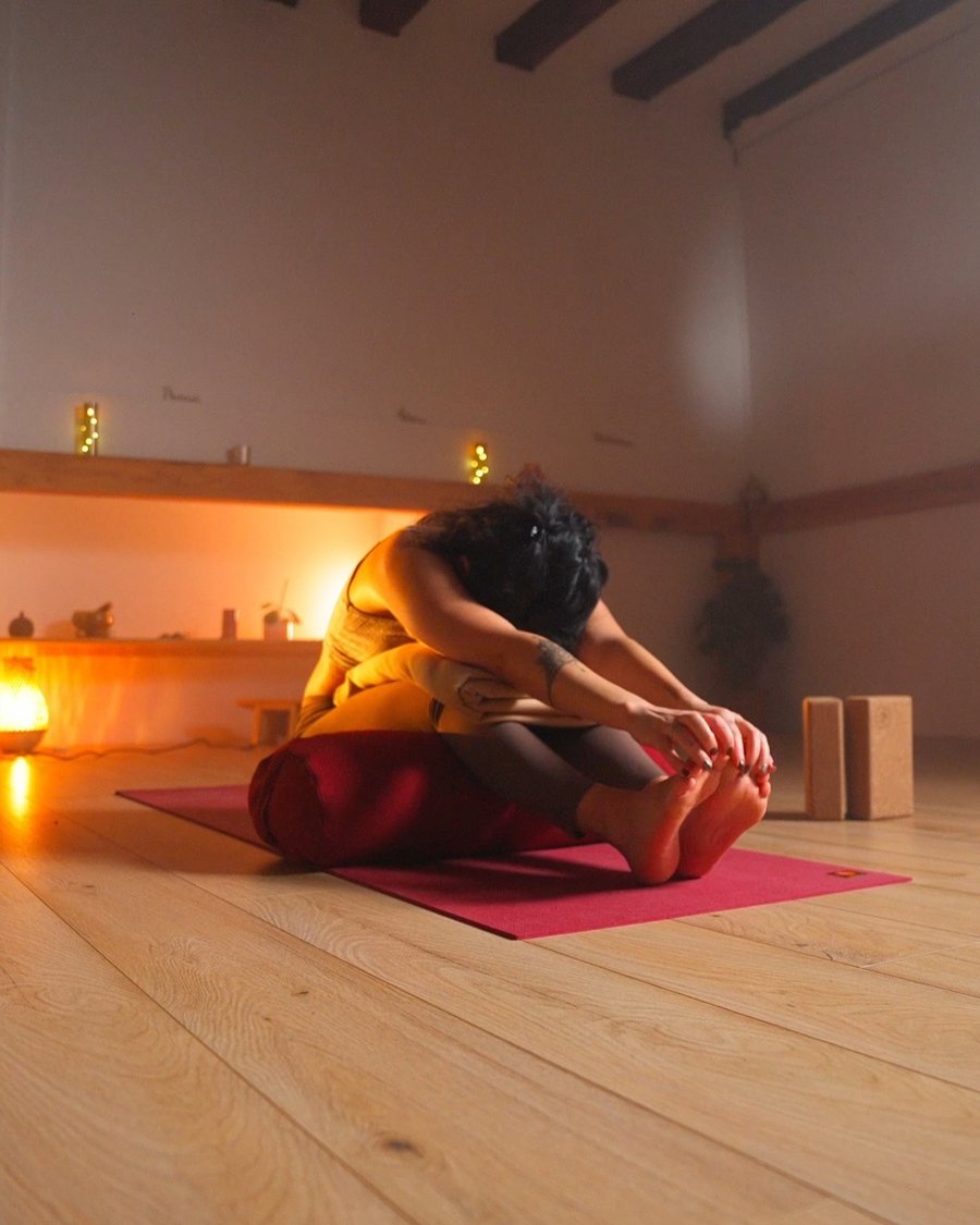 Posture de yoga assise, en flexion avant, dans la lumière chaude de la salle